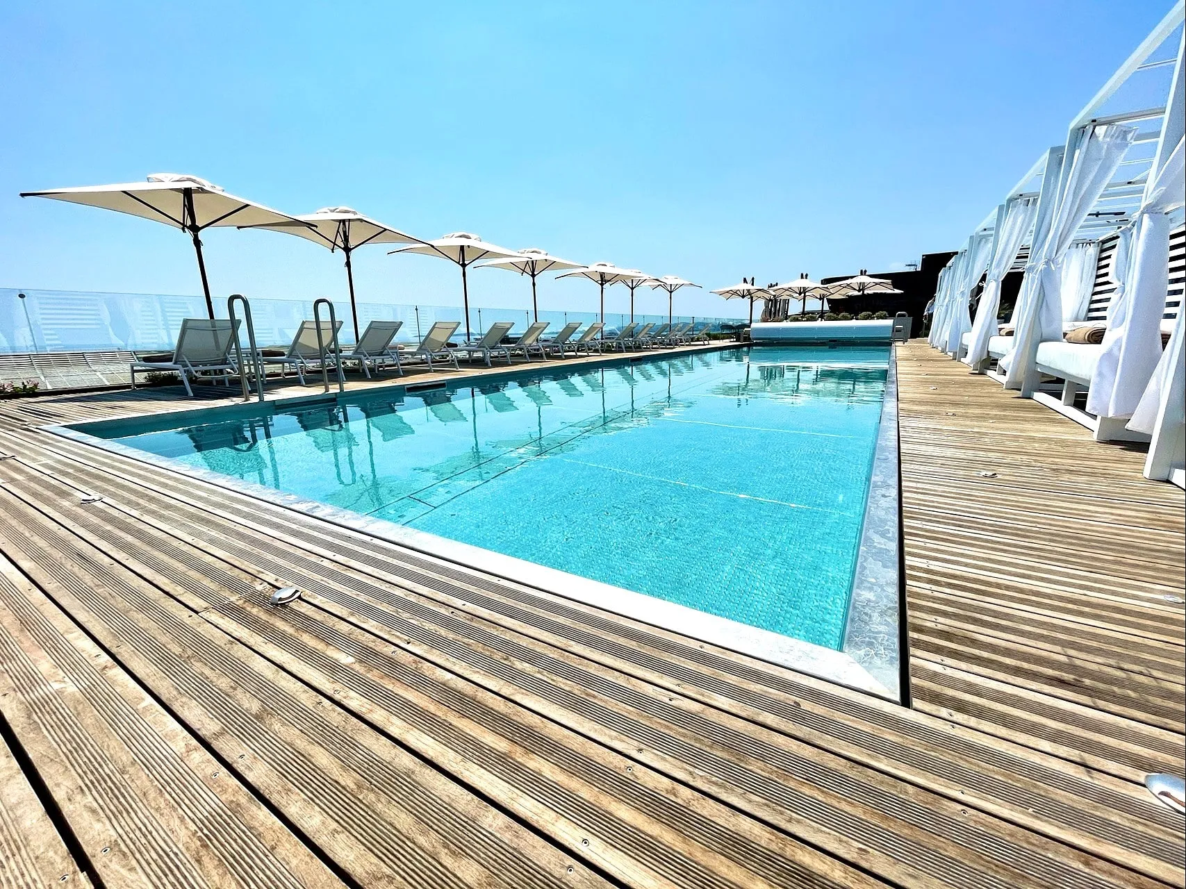 Piscine en inox sur le toit du Sheraton Nice Airport, bordée d'un deck en bois et de parasols, face à la mer.